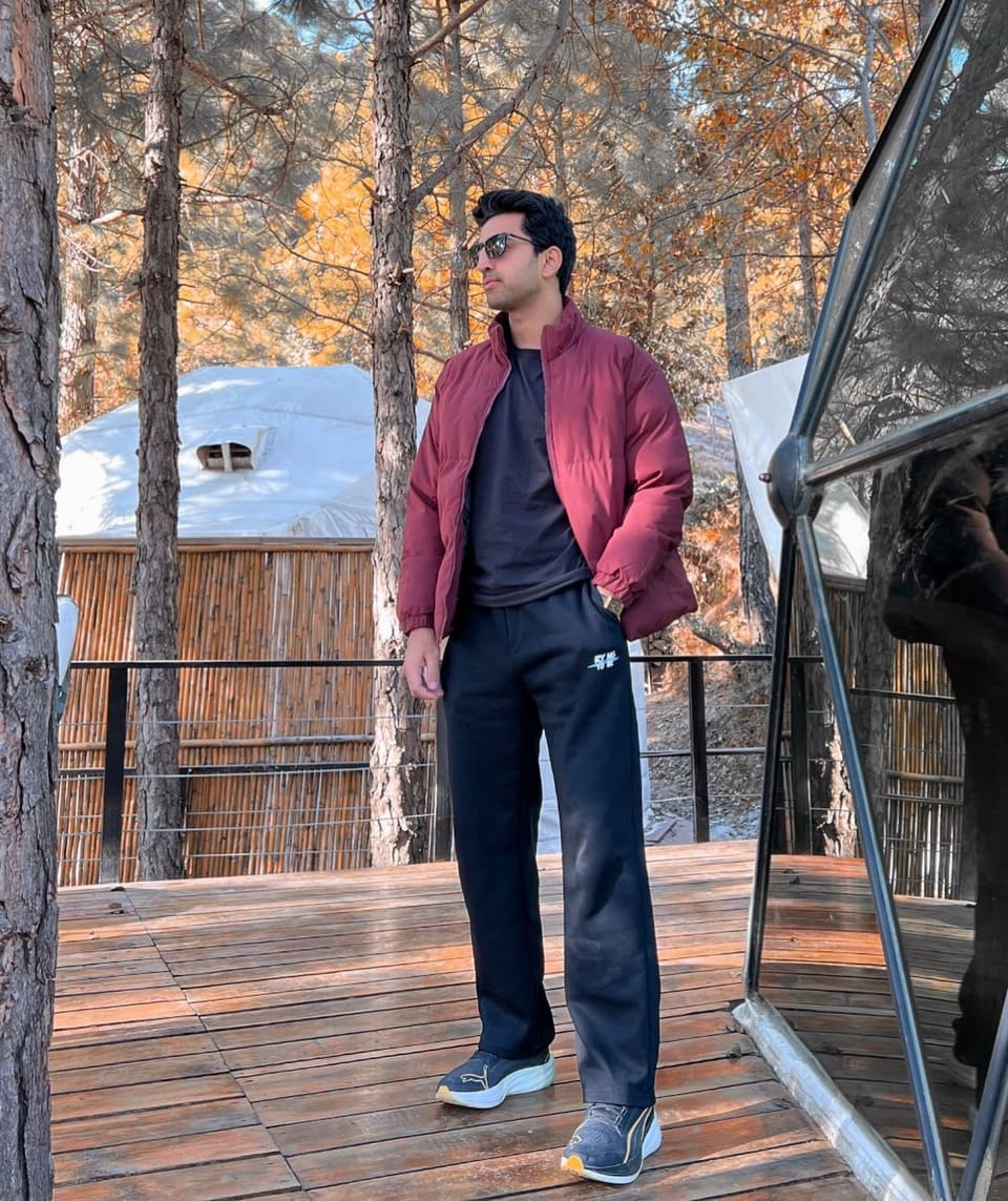 Malik Hamza Javed standing on a wooden deck among autumn pine trees